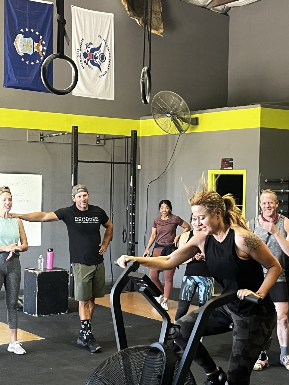 Member digging hard on the air bike with a coach cheering her on