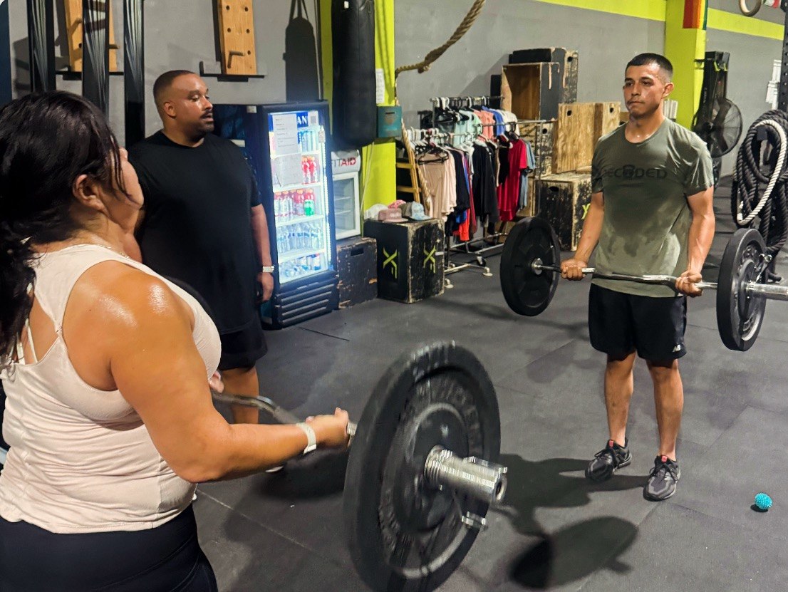 Member working a loaded barbell with a coach spotting her form