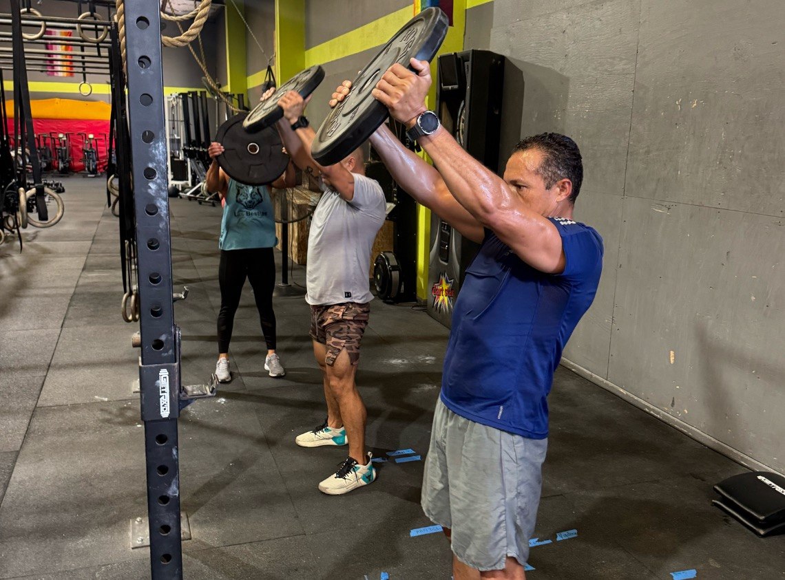 Members pressing bumper plates overhead down the line
