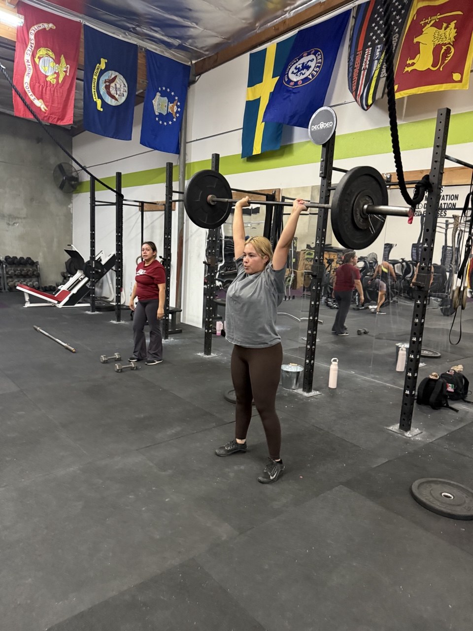 Member pressing a barbell overhead by the flags