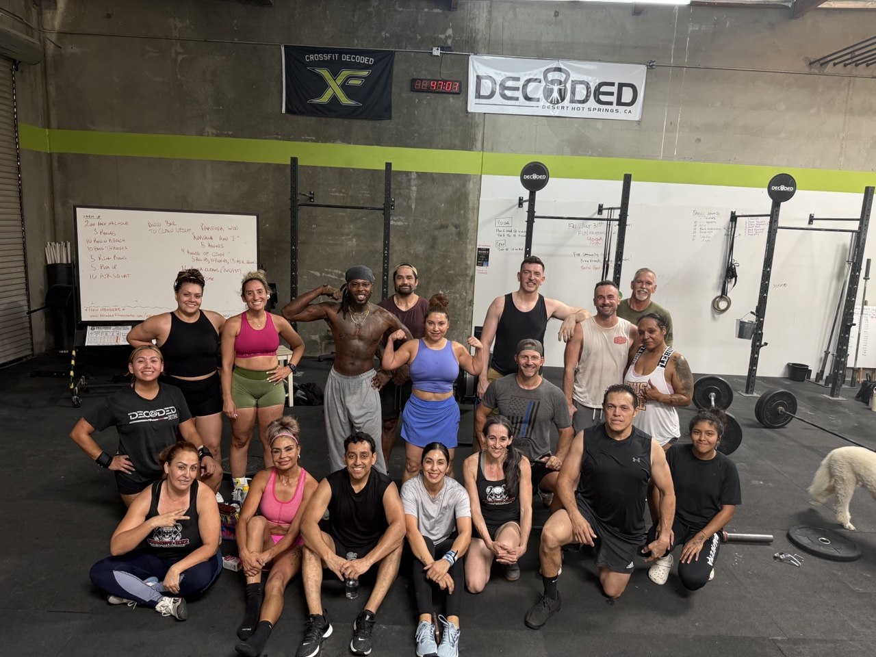 Big group photo of members and coaches after a workout, Decoded banner and CrossFit Decoded flag on the wall behind them