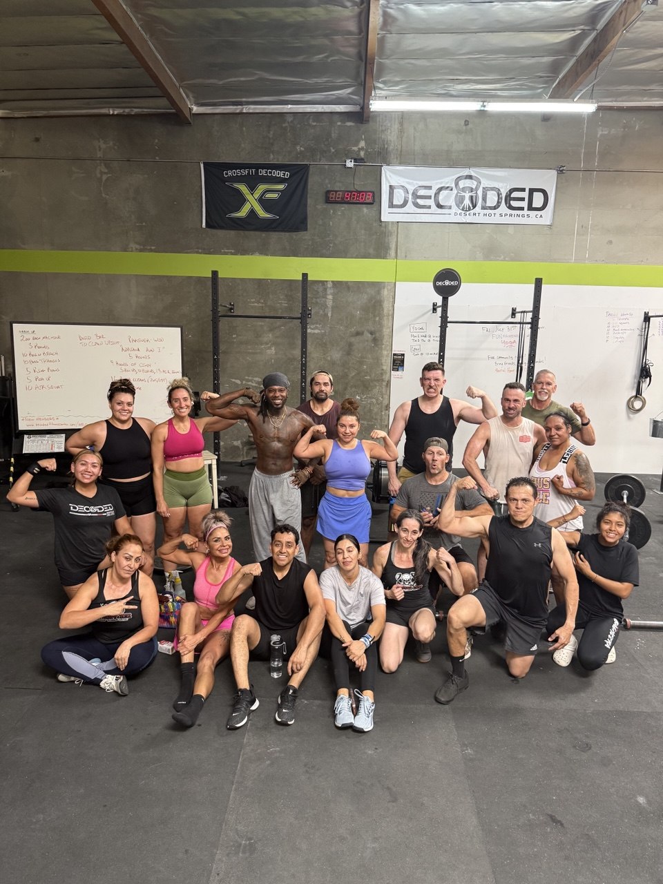 Group of members flexing and smiling together after class under the CrossFit Decoded flag